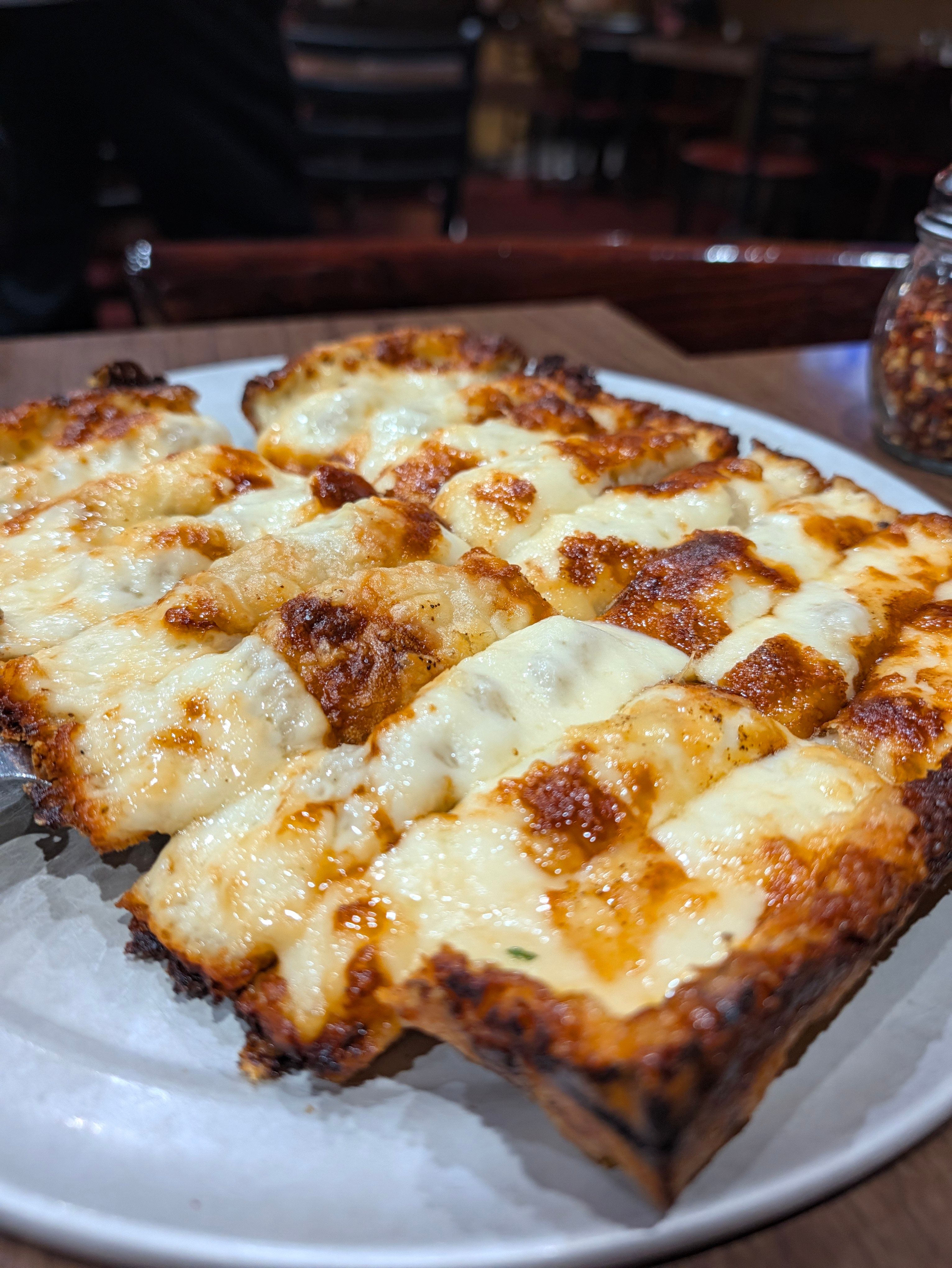 Cheese Bread cut into strips with browned, bubbly cheese on a white plate