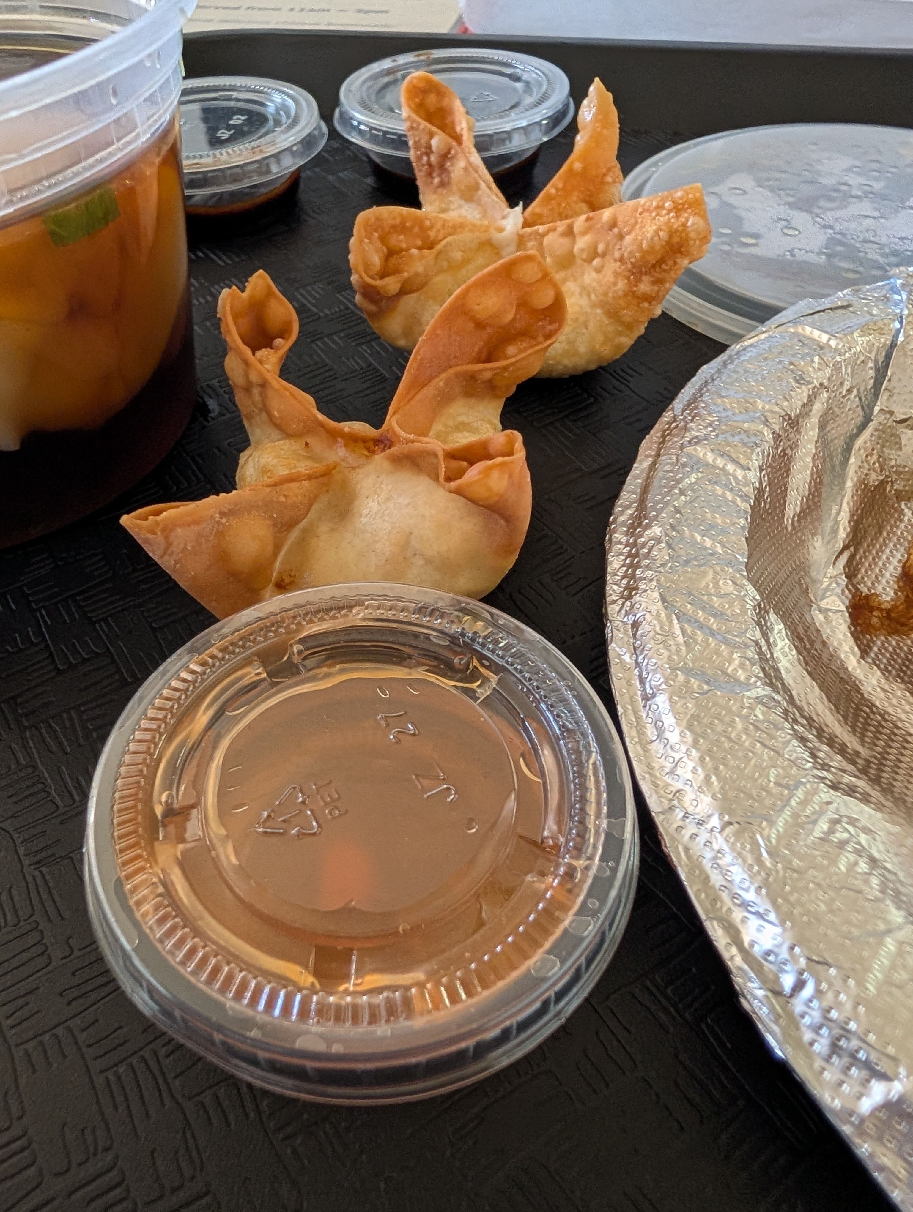 Two golden cheese rangoon with sauce cups on a black tray