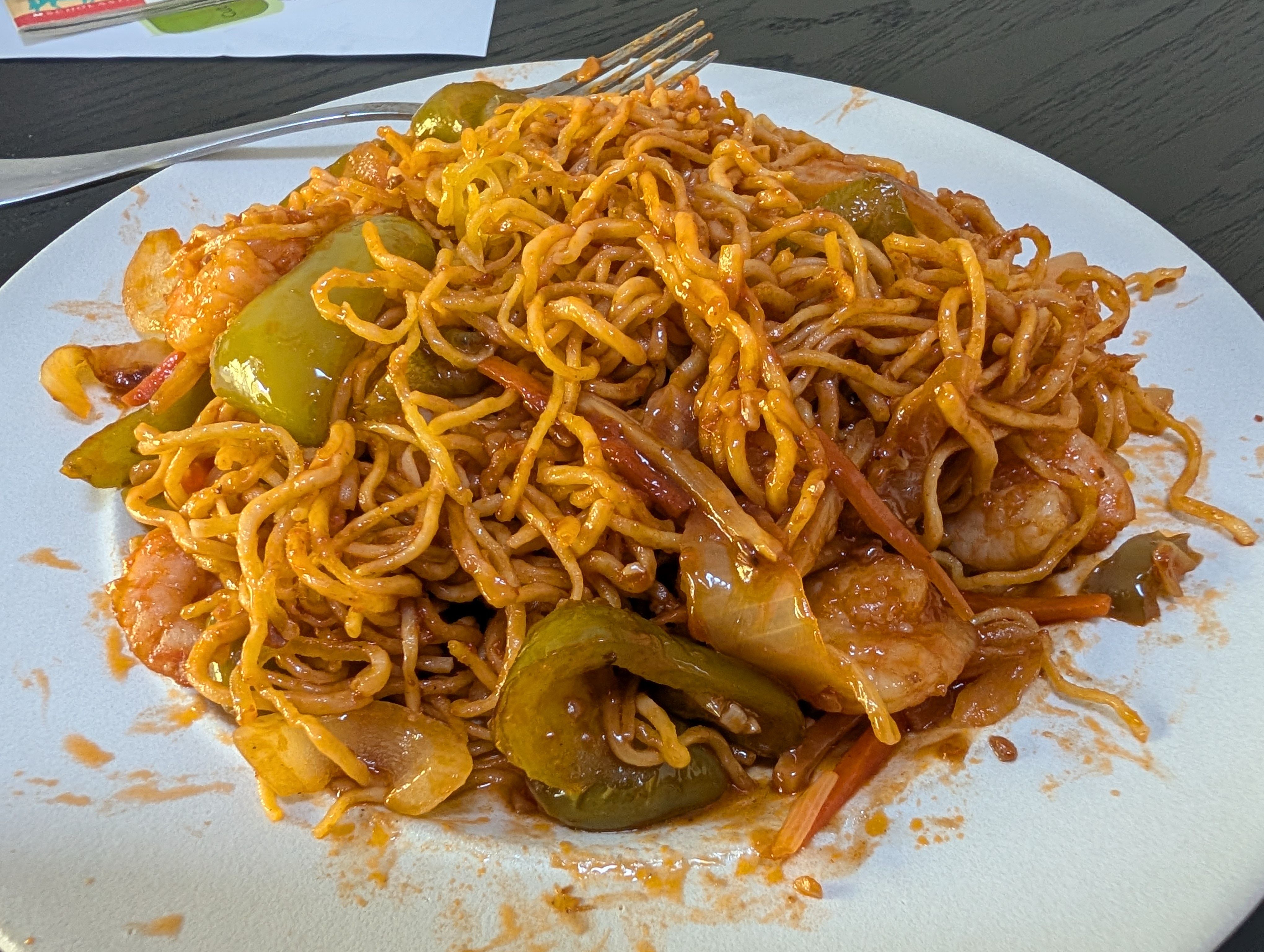 A plate of shrimp chow mein with green pepper, onion and carrot in a red sauce