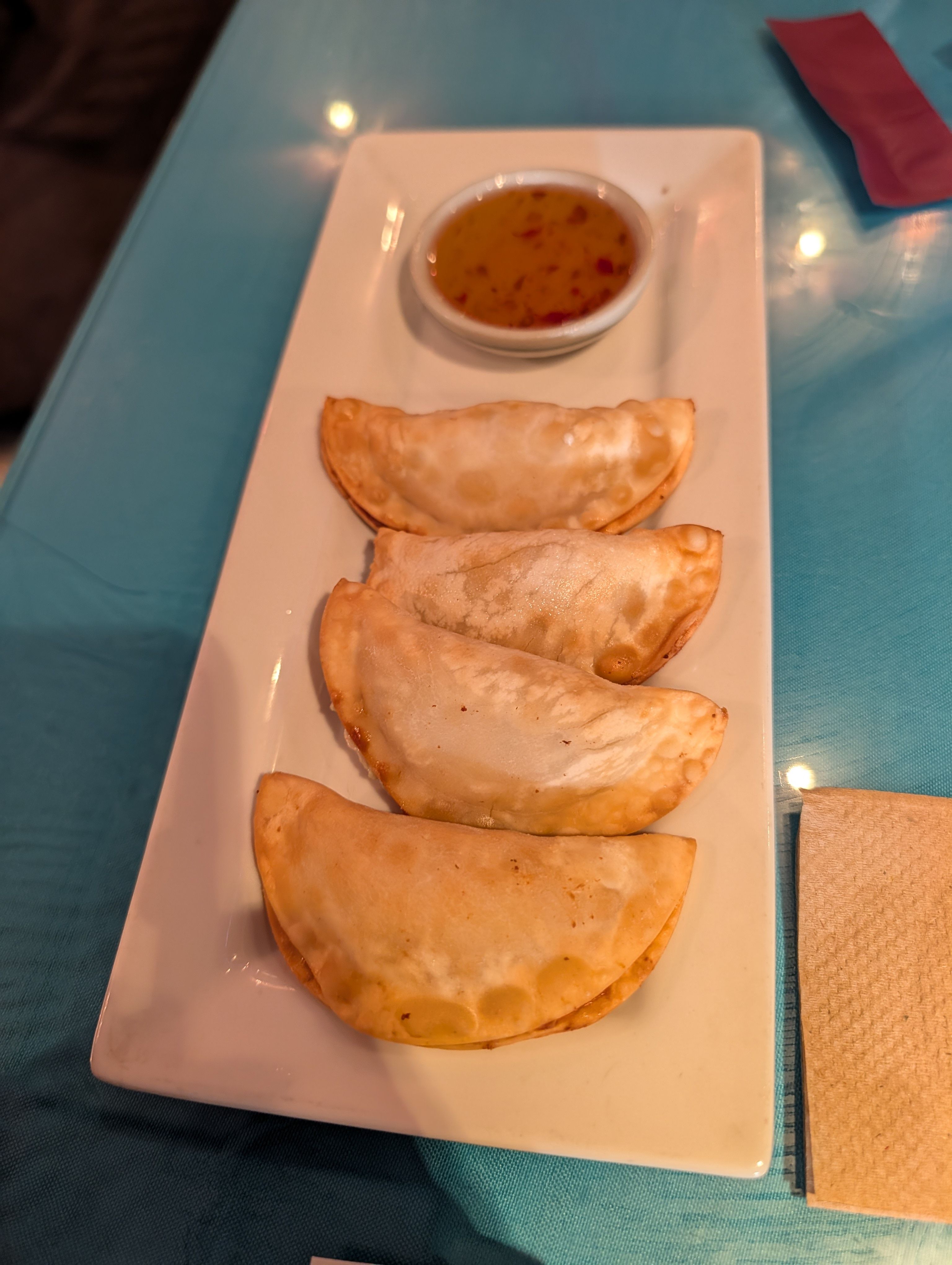 Four fried crab rangoons on a white plate with a dish of sweet chili sauce
