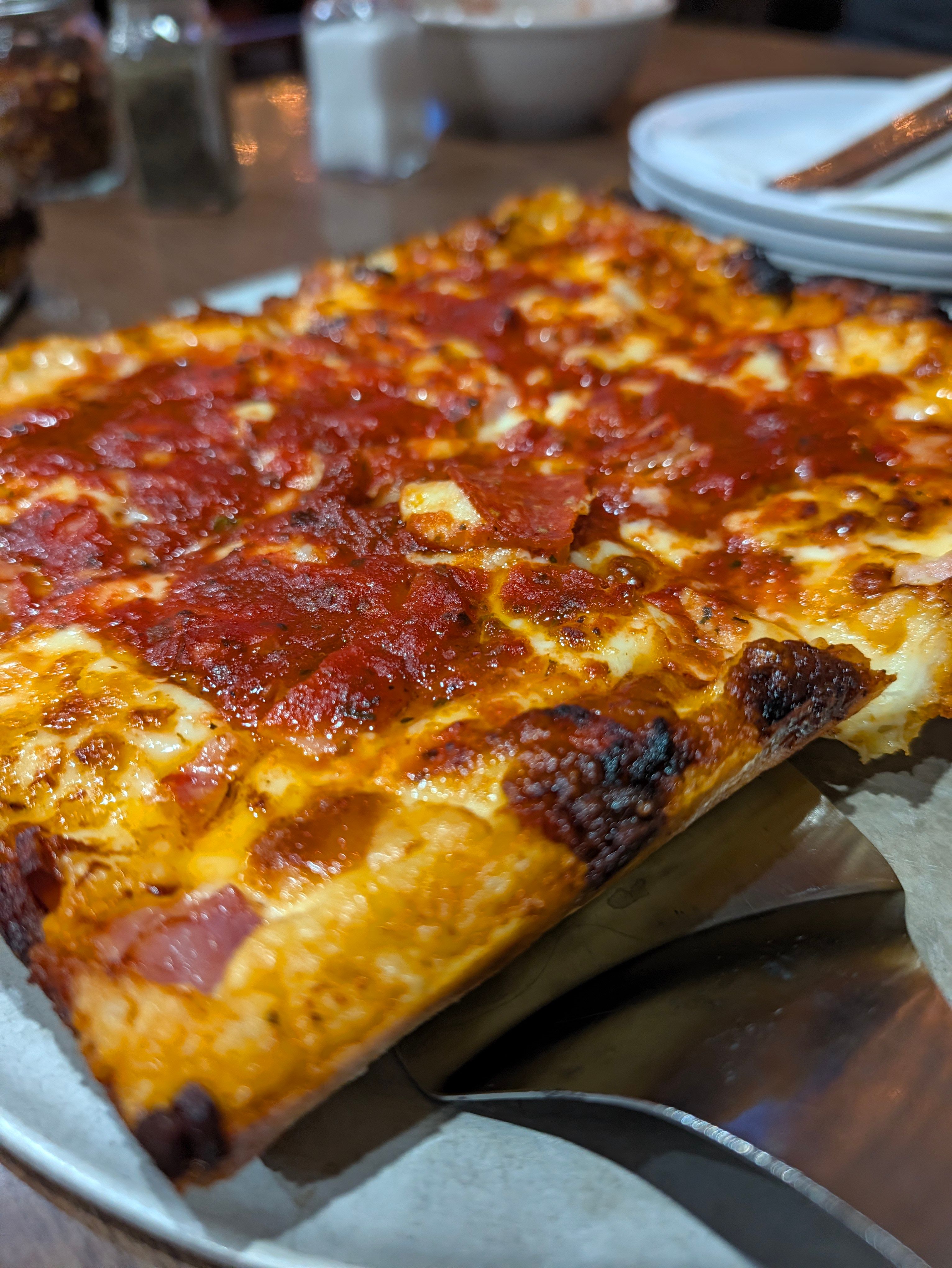 Close-up of a Detroit-style pizza with ham and pepperoni under red sauce and browned cheese