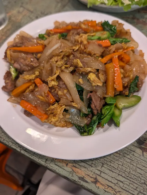 Pad see ew with beef, wide rice noodles stir-fried with egg, carrot batons, and Chinese broccoli on a white plate at Kacha Thai Market