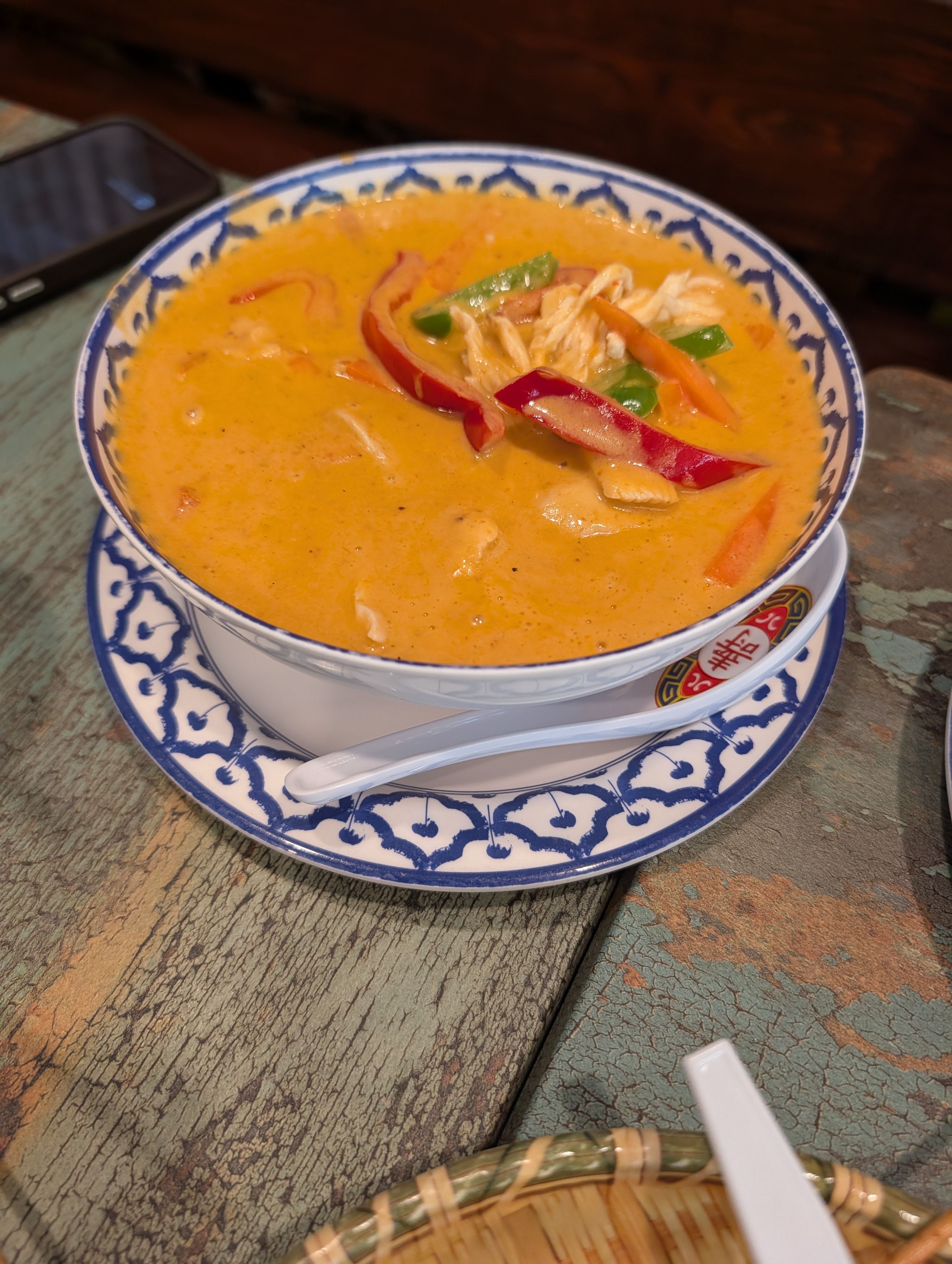 Creamy orange Panang curry with shredded chicken and red and green peppers in a blue and white Thai bowl