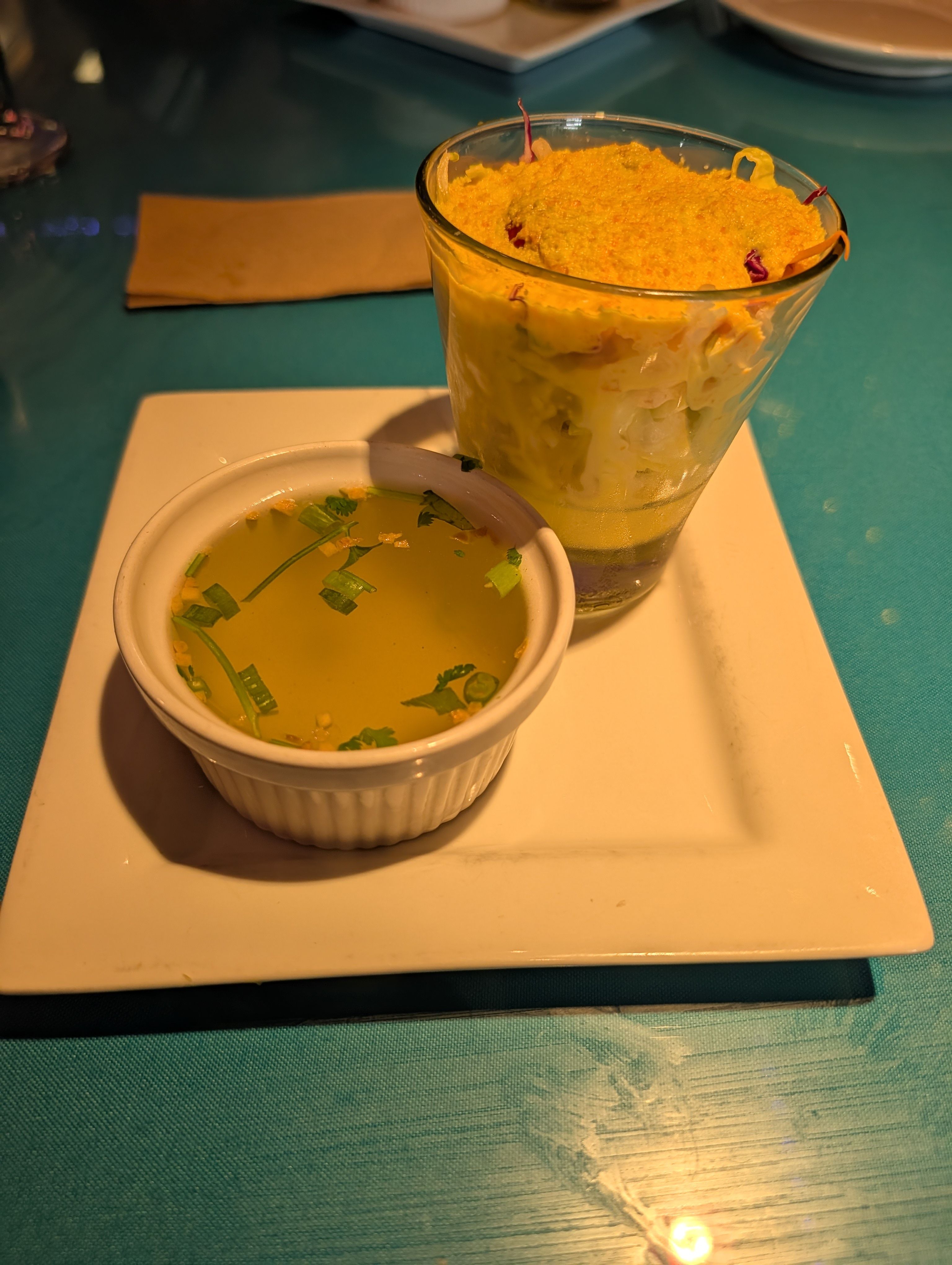 A glass of salad with creamy ginger dressing next to a small ramekin of clear broth
