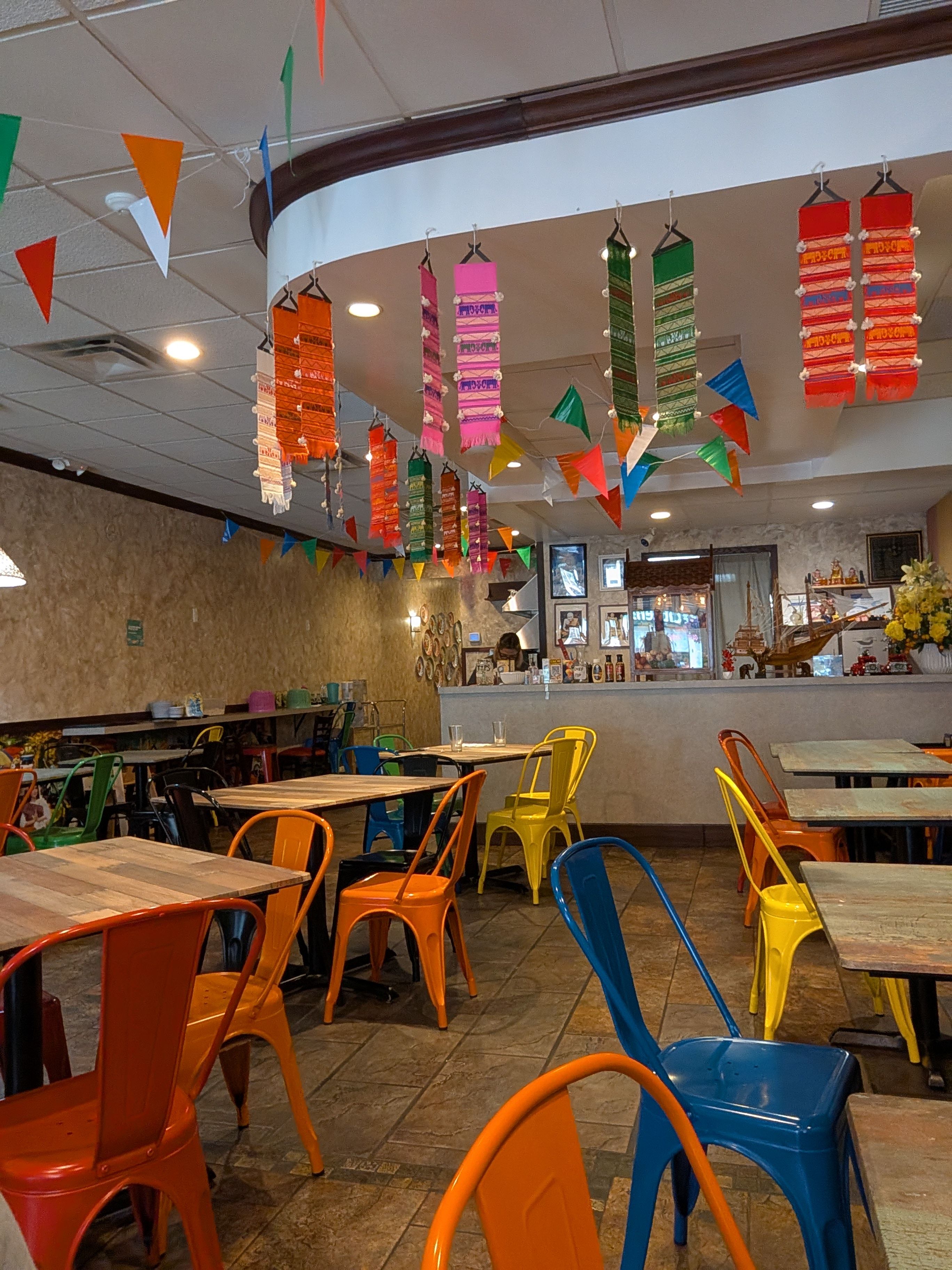 Kacha Thai Market dining room with colorful metal chairs, wood tables, tile floor, and Thai banners hanging from the ceiling