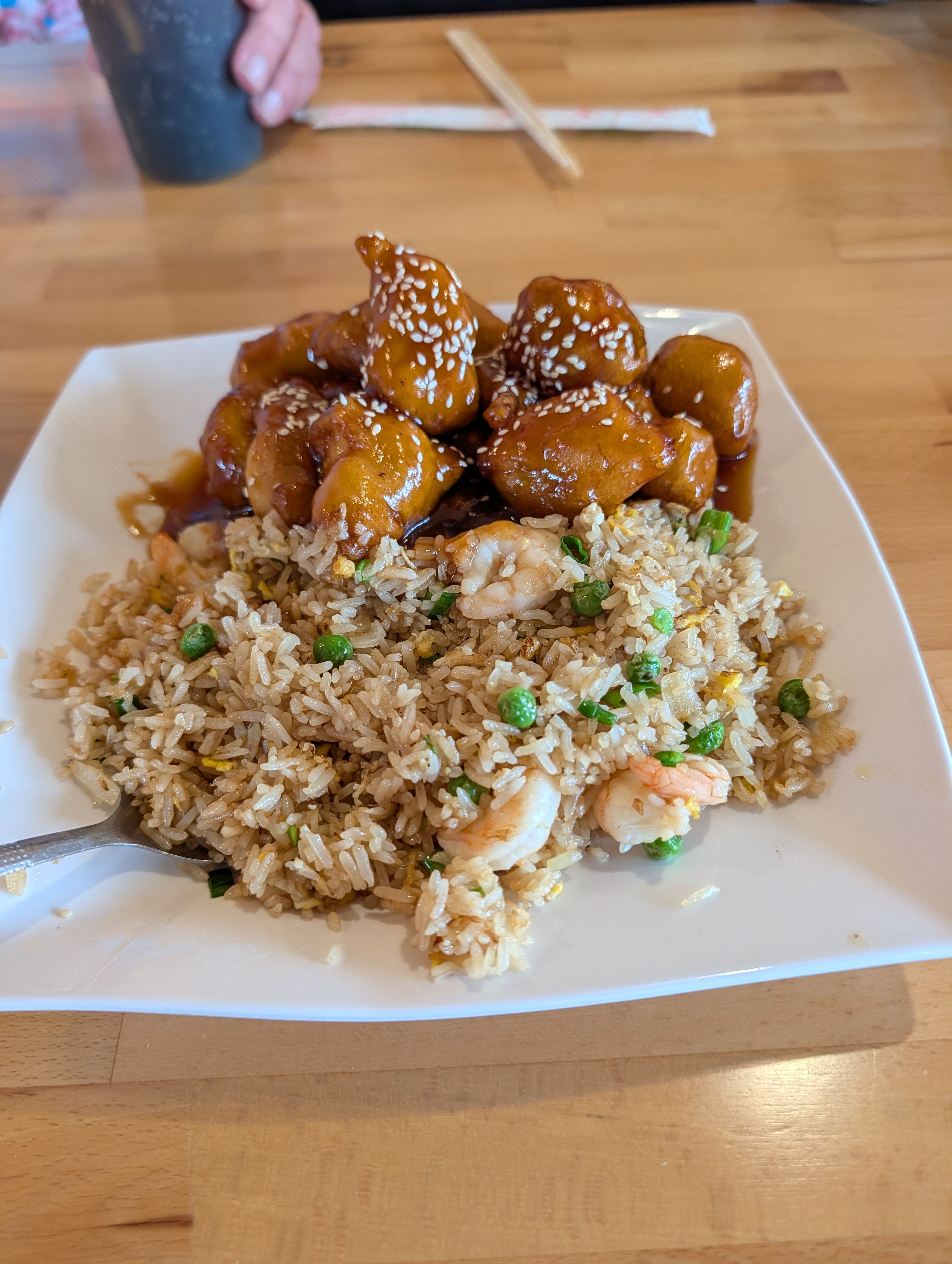 Glazed, sesame-topped chicken beside shrimp fried rice on a white plate