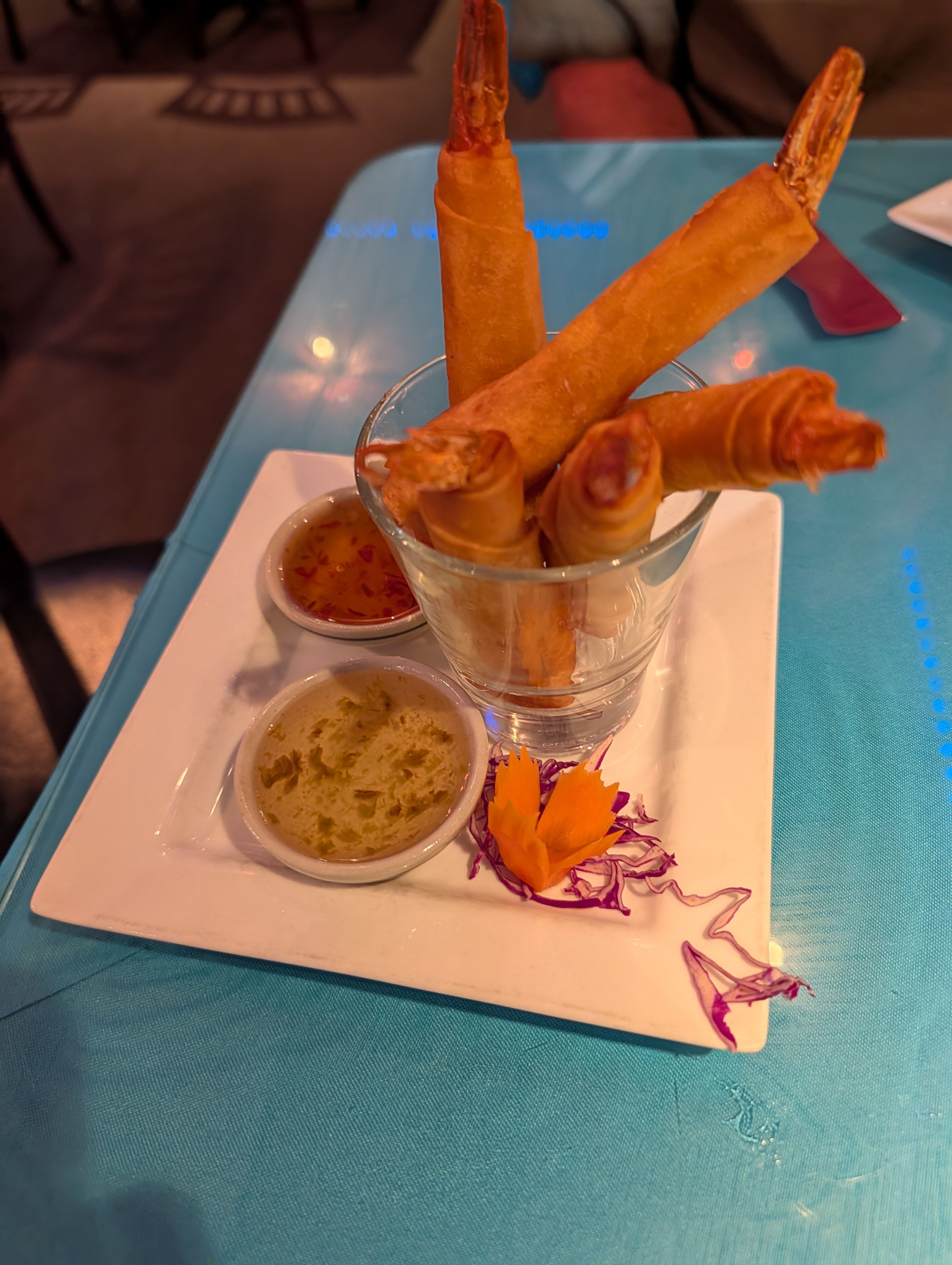 Fried shrimp standing upright in a glass with two dipping sauces and a carved carrot garnish