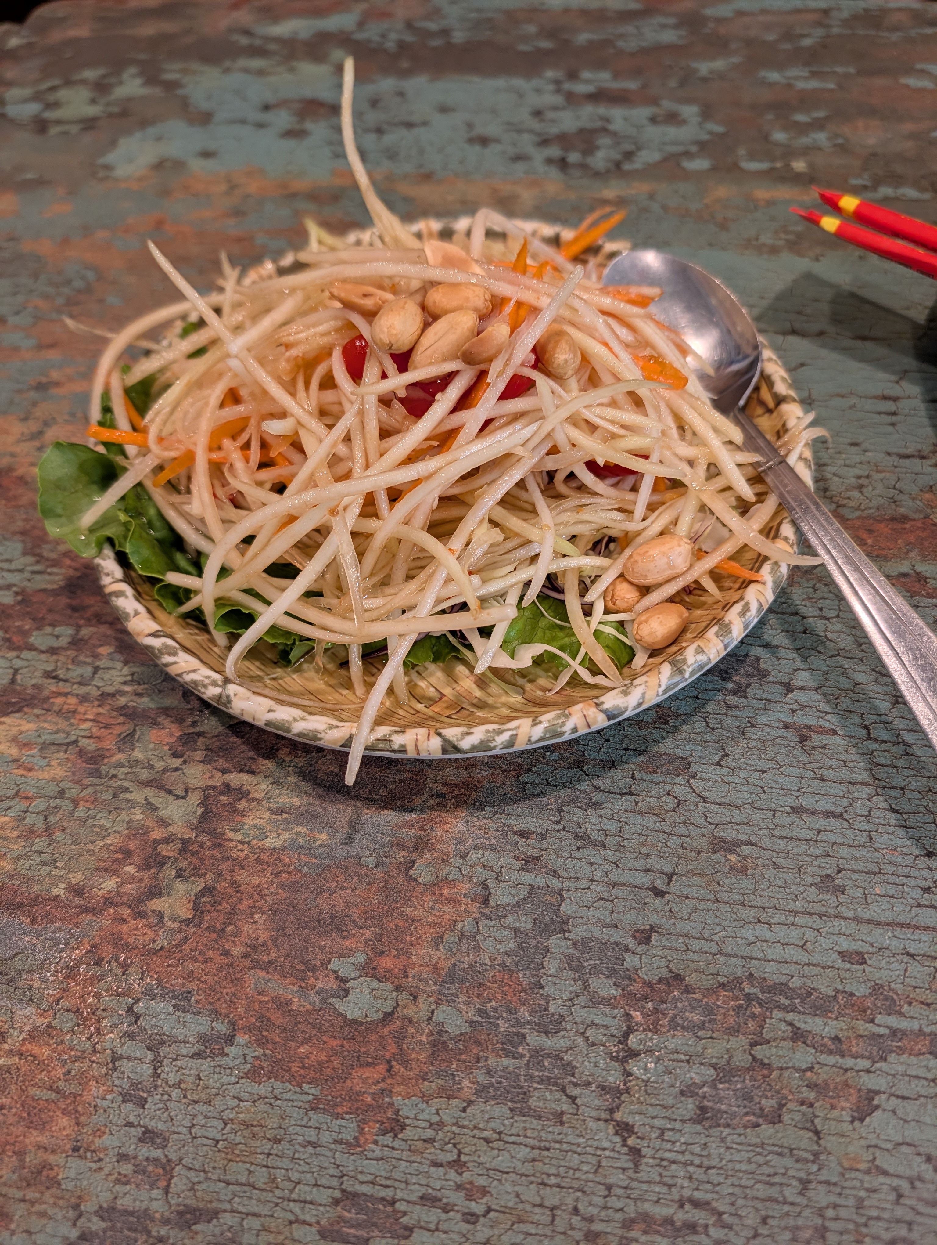 Green papaya salad with shredded papaya, carrot, tomato, and peanuts on a woven basket plate