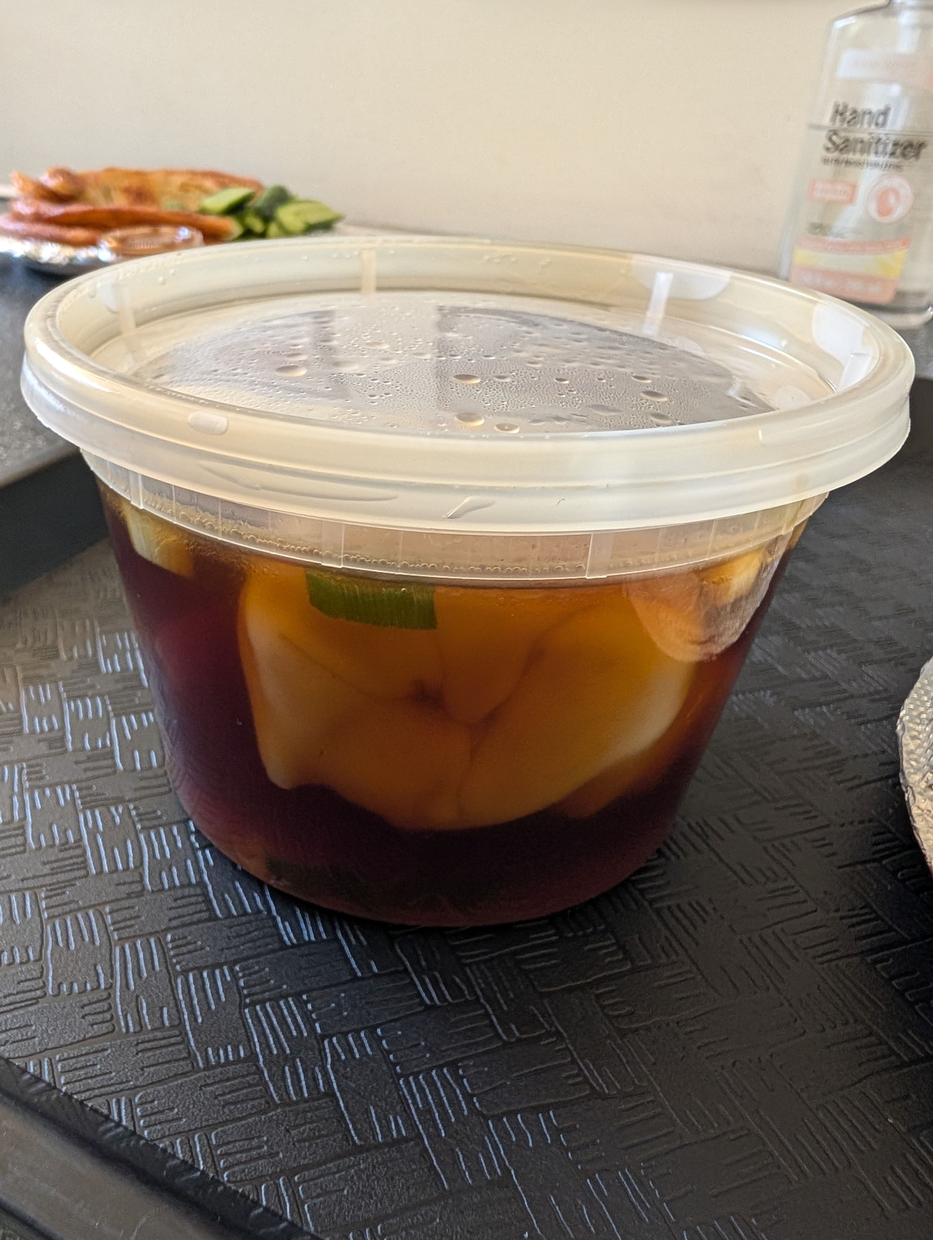 A lidded quart container of wonton soup with pale wontons visible in dark broth